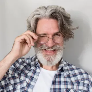 Älterer Mann mit grauem Bart lacht und richtet seine Brille