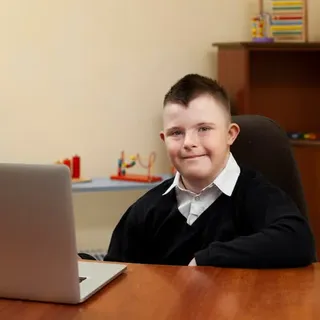 Junge mit Down-Syndrom sitzt lächelnd am Laptop