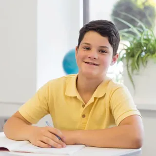 Junge im gelben Poloshirt am Schultisch